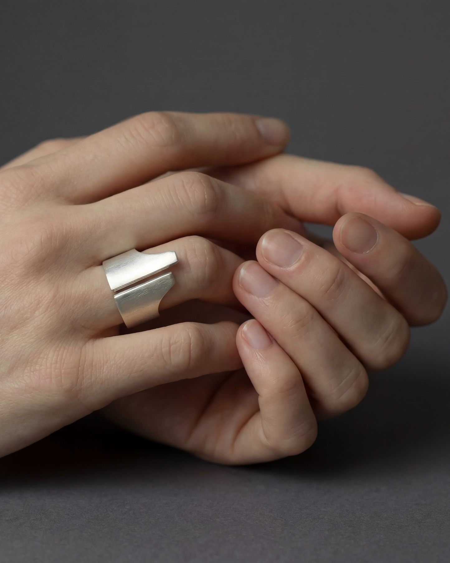 Close-up of a hand wearing a silver ring on a dark background