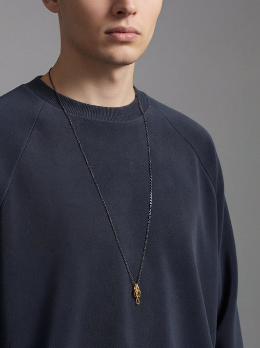 Man wearing a dark blue sweater with a gold necklace against a gray background